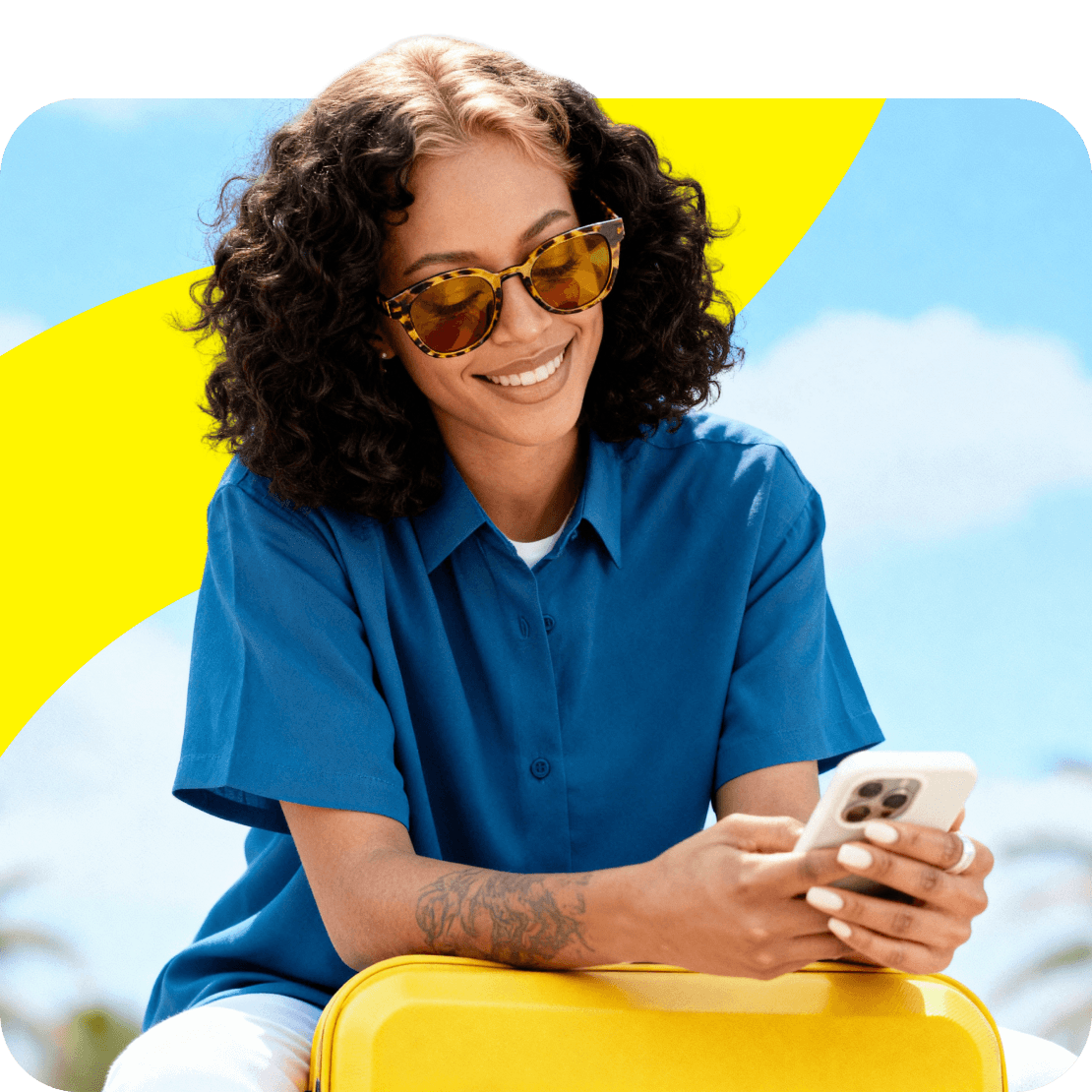 A smiling woman using her phone while sitting with her luggage.