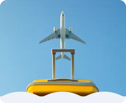 黄色いスーツケースと、その上を飛ぶ飛行機。