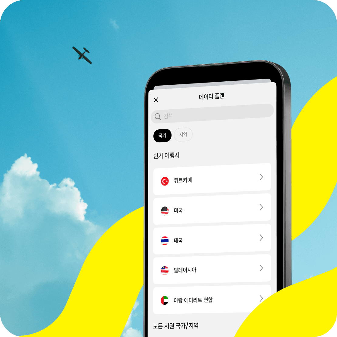 Saily eSIM 앱과 지원 여행지가 표시된 핸드폰 화면, 그 뒤로 푸른 하늘을 배경으로 날아가는 비행기의 모습.