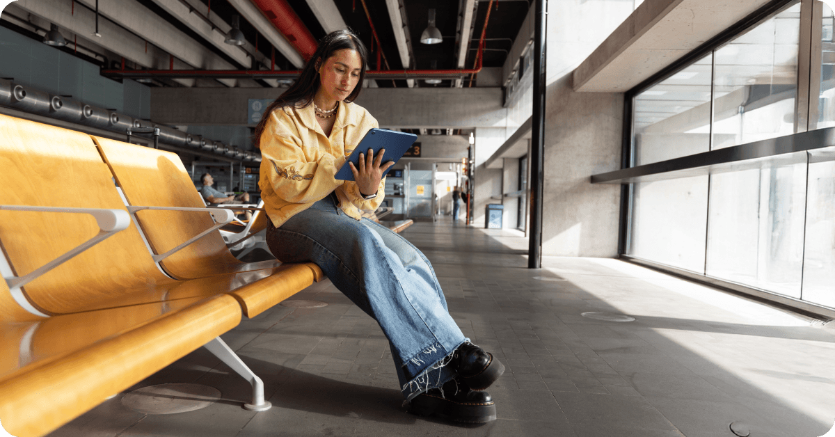 乗り継ぎ空港でのフライトを待つ間、タブレットで情報を確認する女性。